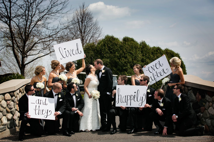 Bride, groom and their wedding party holding signs that say "and they live happily ever after!" At Rush Creek Golf Course in Maple Grove, MN.