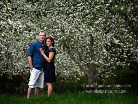 Minnesota Harvest Apple Orchard engagement portraits of Nolan and Amanda standing in the middle of the orchard with the apple trees in full bloom. Engagement image taken in Jordan, Minnesota.