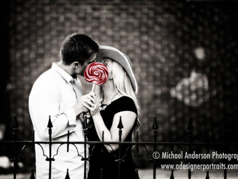 A cute couple kissing behind a red lollipop during one of their fun engagement portraits in Stillwater, MN.