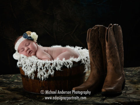 Maternity and newborn portraits of Bralynn Ra sleeping in a barrel with cowboy boots by her side.