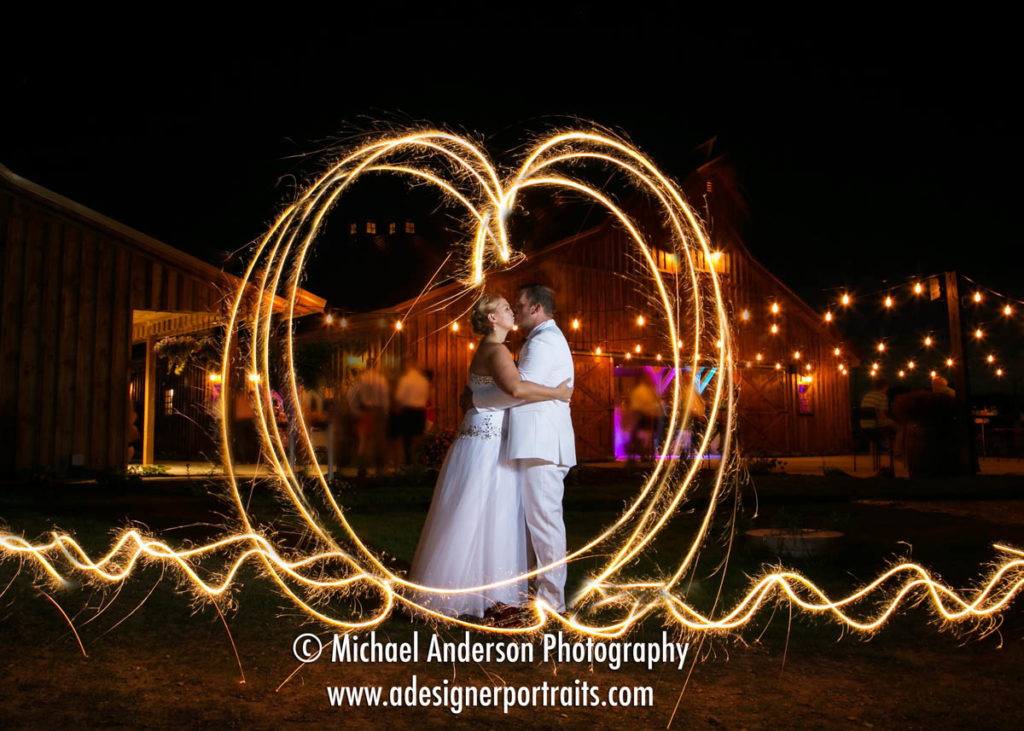 Night wedding photo of a bride & groom kissing in a heart made from sparklers. Image taken at The Hitchin' Post wedding of Jay & Vanessa in New Richmond, WI.