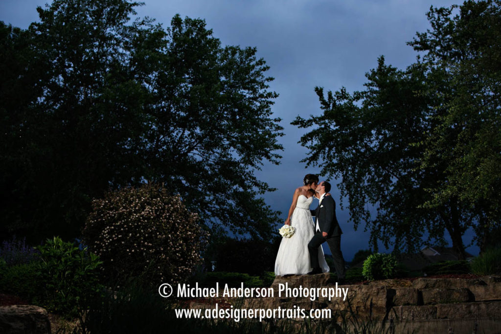 Minneapolis Wedding Photographers. Beautiful wedding photograph of a bride and groom kissing on a stone bridge. Image taken at night at TPC Twin Cities in Blaine, MN.