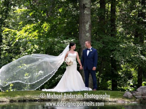 A very pretty wedding photograph of the bride and groom with her veil flowing in the wind; Image taken by a pretty pond before their Grand View Lodge destination wedding.