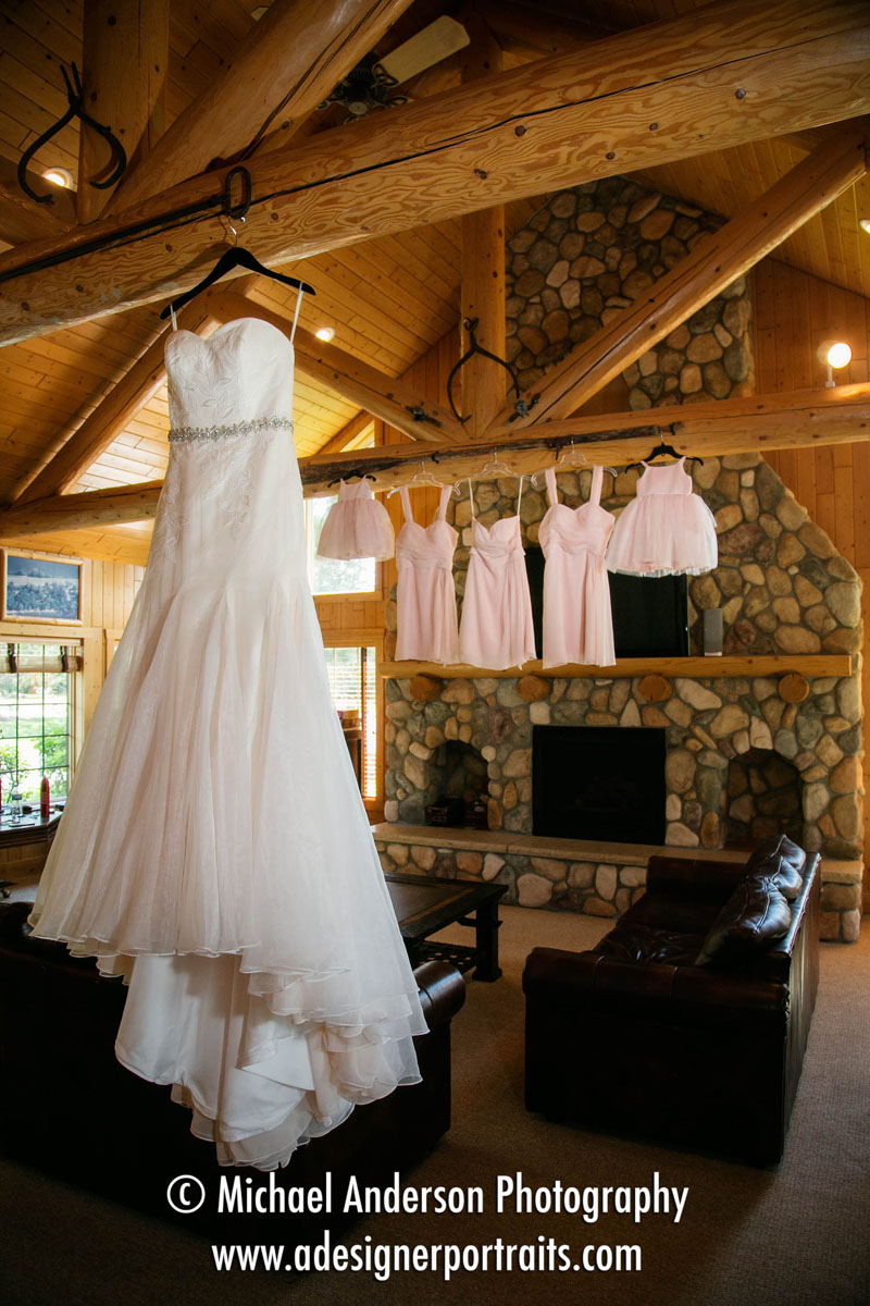 Wedding details photo of the bride's pretty dress and her bridesmaids and flower girl's dresses too. Dresses are hanging from the log rafters at an Interlachen, part of Grand View Lodge in Nisswa, MN.