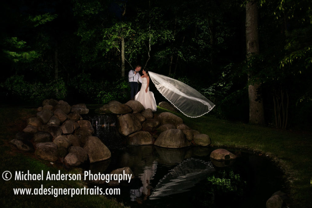 A Pretty light painting wedding photo of the bride & groom with her veil flowing in the breeze. Destination wedding photography created at the waterfall and pond at Grand View Lodge in Nisswa, MN.