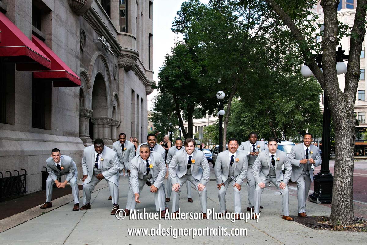 The groom and his fellow college football groomsmen strike a pose in a football formation outside of the Landmark Center in Saint Paul, MN.