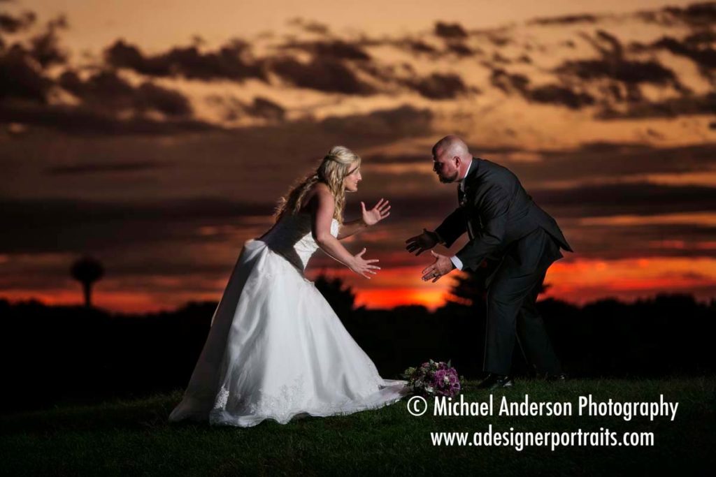 Wedding photography at The Wilds Golf Club Prior Lake MN. Bride & groom, a former wrestler, strike a wrestling pose in front of a beautiful sunset at their wedding reception at The Wild's Golf Club in Prior Lake, MN.
