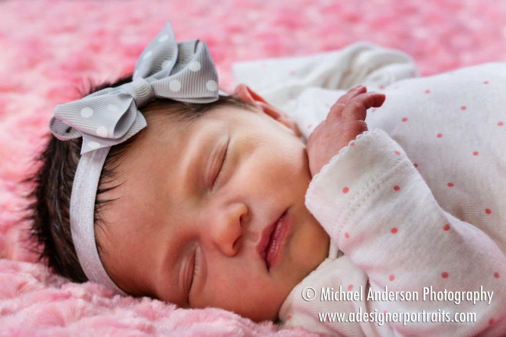 A cute studio portrait of a pretty newborn baby girl wearing a pink outfit and a cute headband.