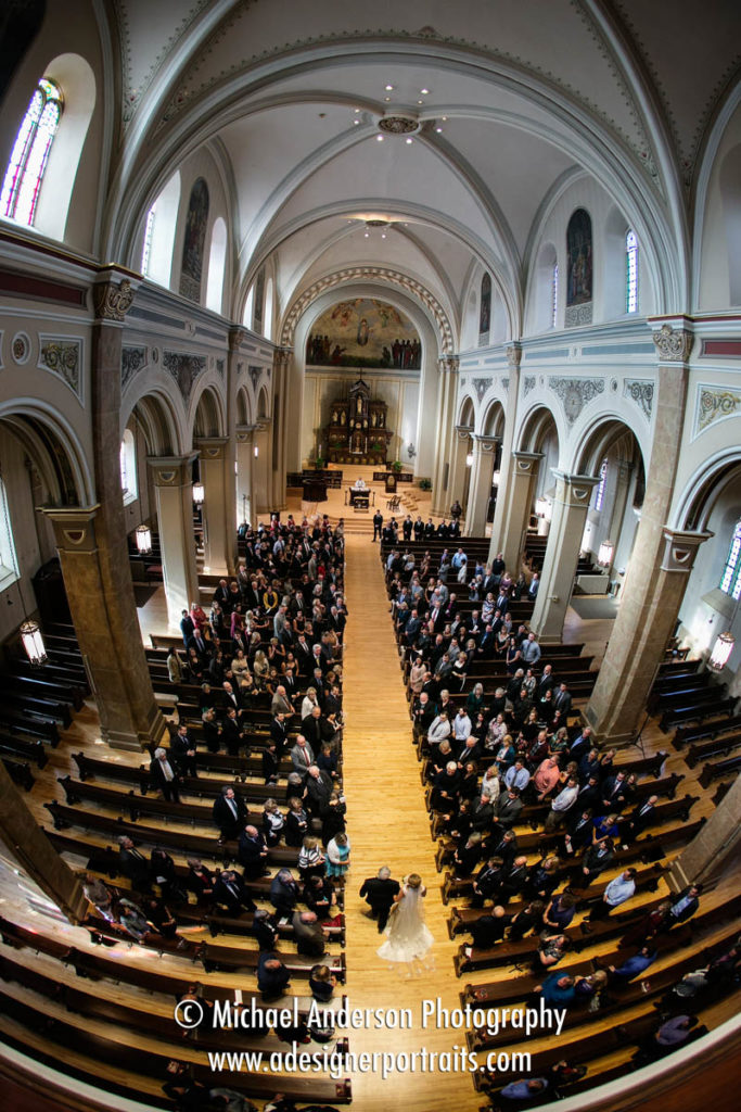 Stunning wedding photograph taken with a fisheye lens from the balcony at Church of the Assumption in St. Paul, MN. Image of the bride and her father walking down the aisle together.