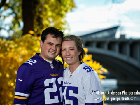 A cute couple wearing their Minnesota Vikings jerseys during their engagement portrait session in the fall colors on St. Anthony Main in Minneapolis, MN.