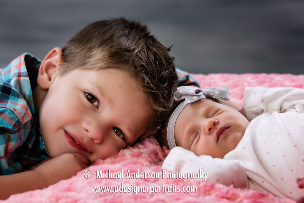 A cute studio portrait of a four year old boy and his new sister, an adorable newborn baby girl.