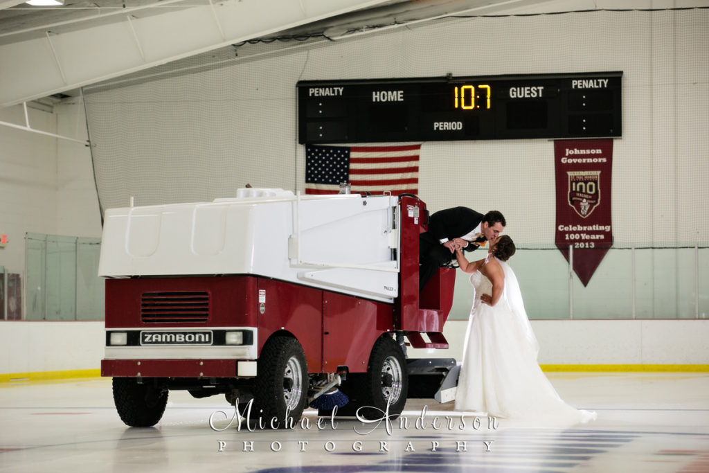 The groom leans over on the Zamboni to share a kiss with the bride on the hockey rink at Saint Paul Johnson High School on the East Side of St. Paul, MN.