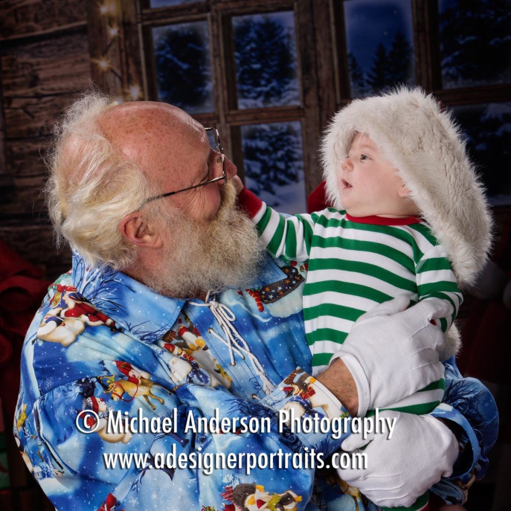 An adorable six month old baby boy tugs on Santa's beard during his Christmas Portraits with Santa Claus 2016.