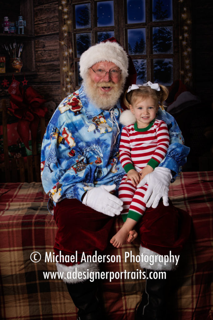 A cute two year old girl sits on Santa's lap during her Christmas Portraits with Santa Claus 2016.