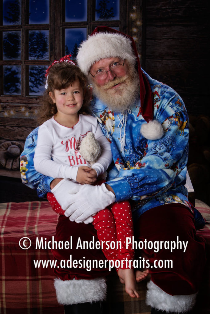 An adorable five year old girl sits on Santa's lap in her Christmas pajamas. Image created during her 2016 Heirloom Santa Photos.