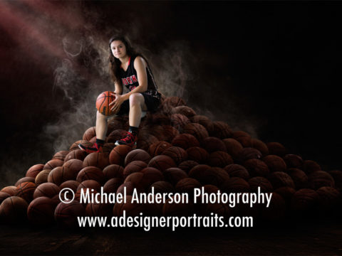 Green screen portrait of a North Saint Paul girls basketball player sitting on a pile of basketballs.