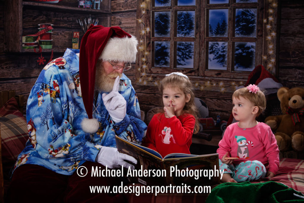 Cute portrait of Santa Claus reads "The Night Before Christmas" to two adorable sisters wearing their Christmas pajamas.