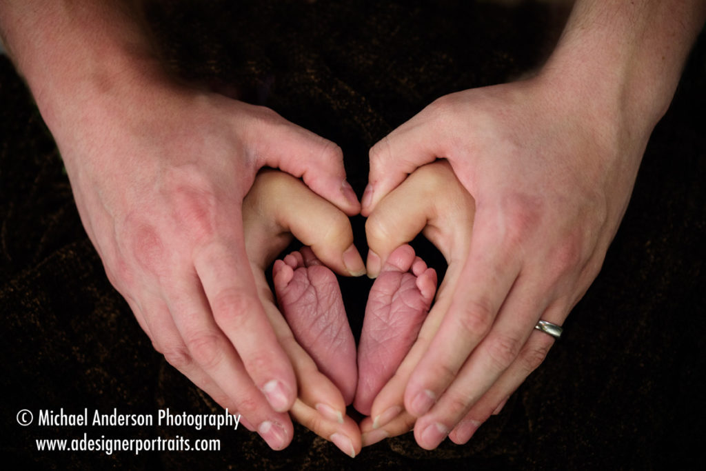 Mom and dad holding their adorable three day old baby boy's feet in their heart shaped hands.