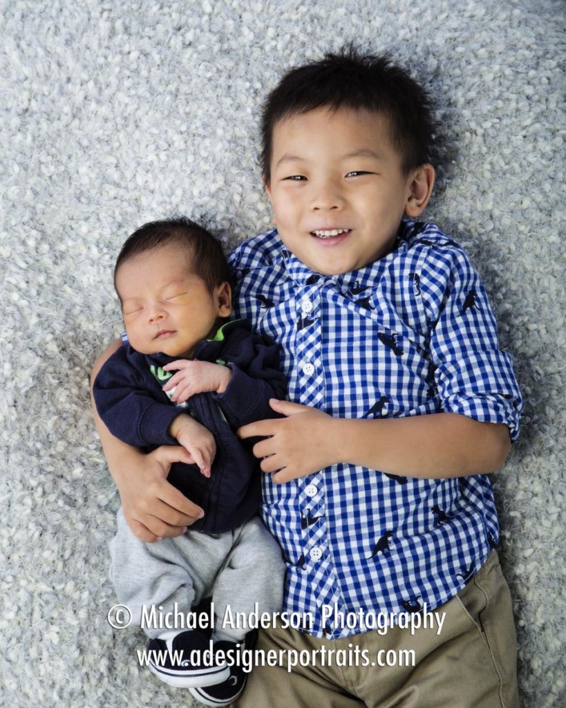 A proud big brother holds on to his new baby brother during his newborn baby portraits.