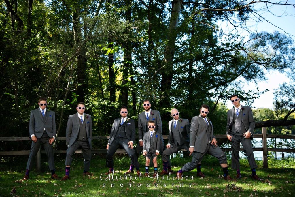 A fun wedding photograph taken at Colby Lake Park in Woodbury, MN. The groom, his four groomsmen and ring bearer are wearing sunglasses and showing off their mismatched socks. 