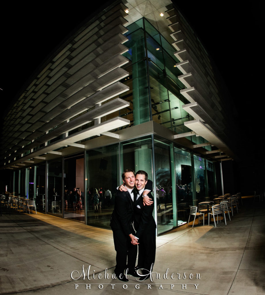 The two grooms pose in a fun, nighttime photo outside during their Orchestra Hall wedding dance.