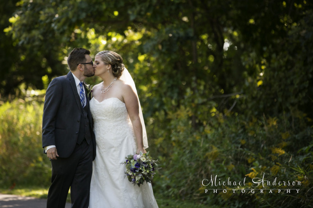 A pretty wedding photograph of a bride and groom walking along a pathway and stopping to kiss. The wedding day image was created at Colby Lake Park in Woodbury, MN.