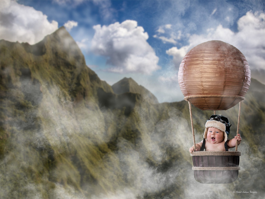 A cute fantasy baby portrait titled "The Little Aviator." An adorable five month old baby boy flying a hot air balloon in the clouds over Maui, Hawaii.