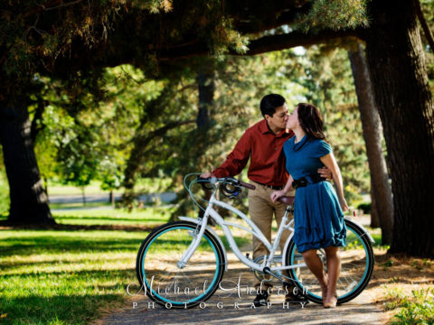 A cute couple sharing a kiss on a white bicycle, in a very pretty setting at Como Park. The very cute image was taken during their Como Park engagement portraits.