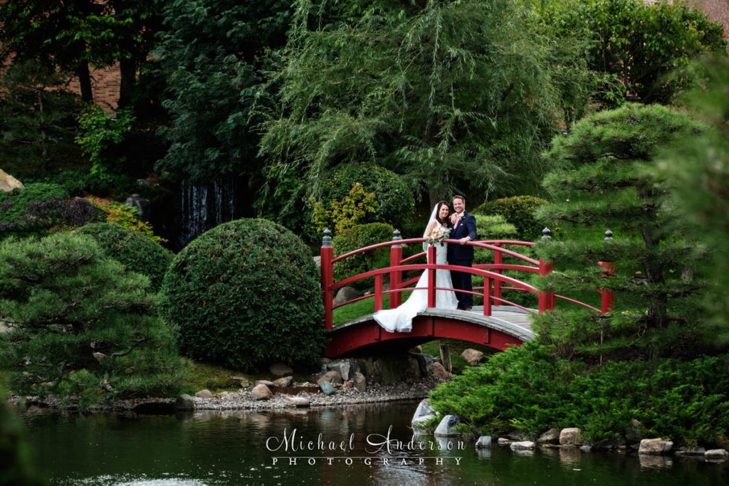 A classic bridal portrait of a bride and groom standing on a red bridge over the pond. Pretty wedding photography at The Japanese Garden at the Normandale Community College in Bloomington, MN.