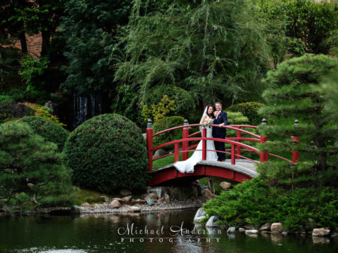 A classic bridal portrait of a bride and groom standing on a red bridge over the pond. Pretty wedding photography at The Japanese Garden at the Normandale Community College in Bloomington, MN.