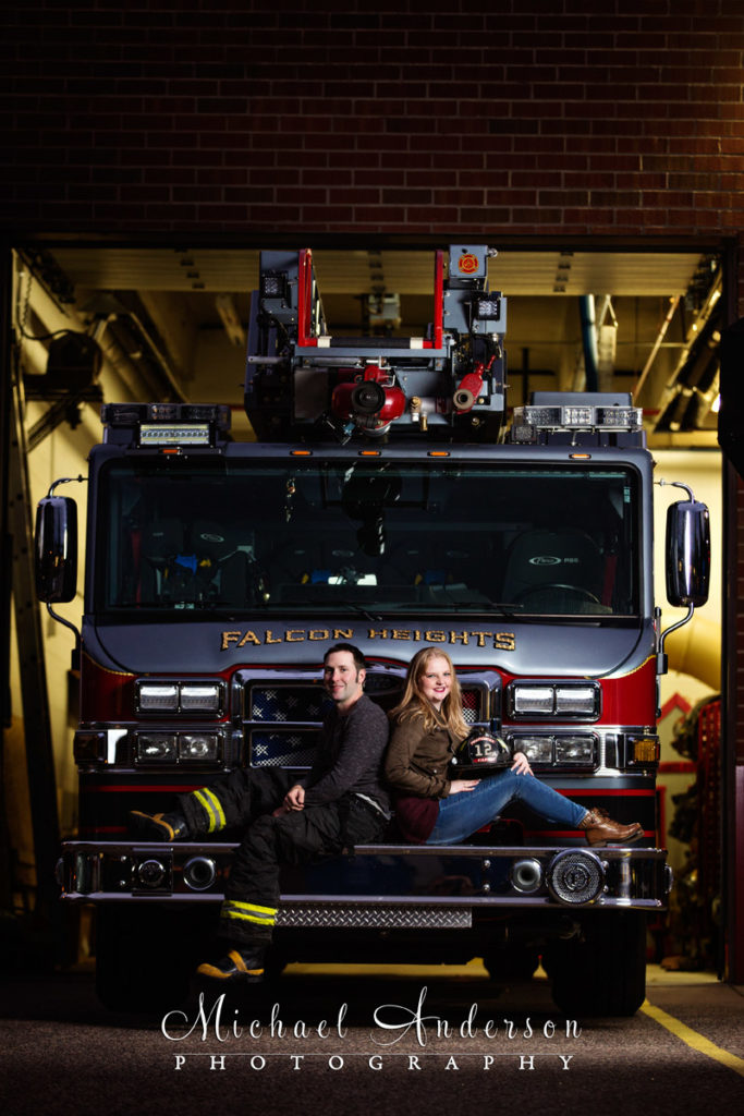 Engagement portrait of Ben and Emilee sitting on the front bumper of Ladder 757 at the Falcon Heights Fire Station.