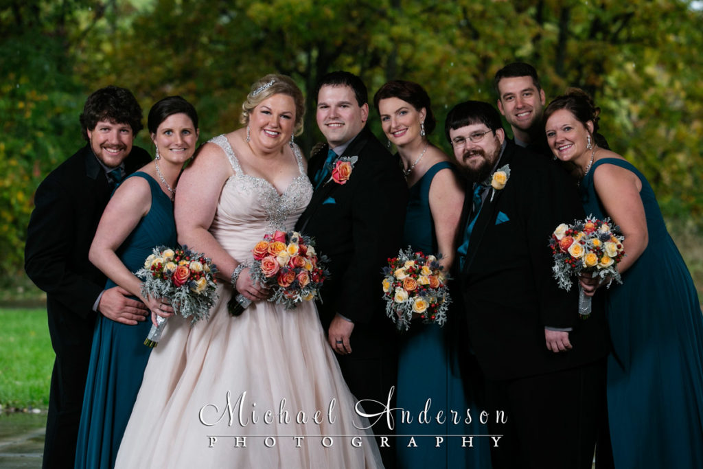A fall color wedding photo of the bride, groom and their wedding party staying dry in a picnic shelter in Eagan, MN on a very rainy day.