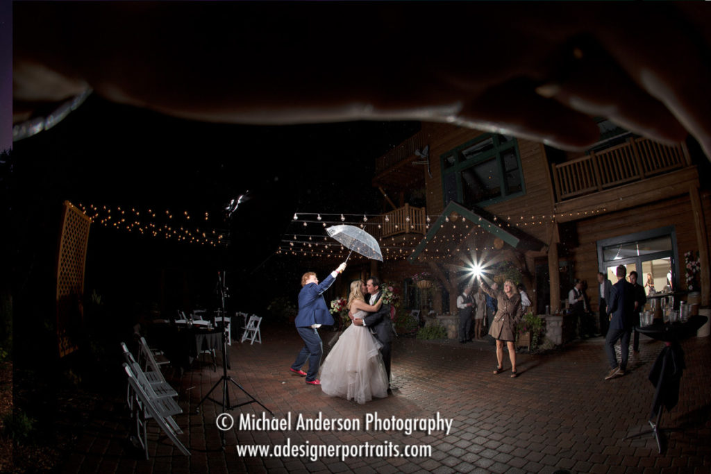 The starting image before any light painting of the bride and groom in the rain at their Grand Superior Lodge destination wedding. The couple is standing under an umbrella on the patio during their wedding dance.