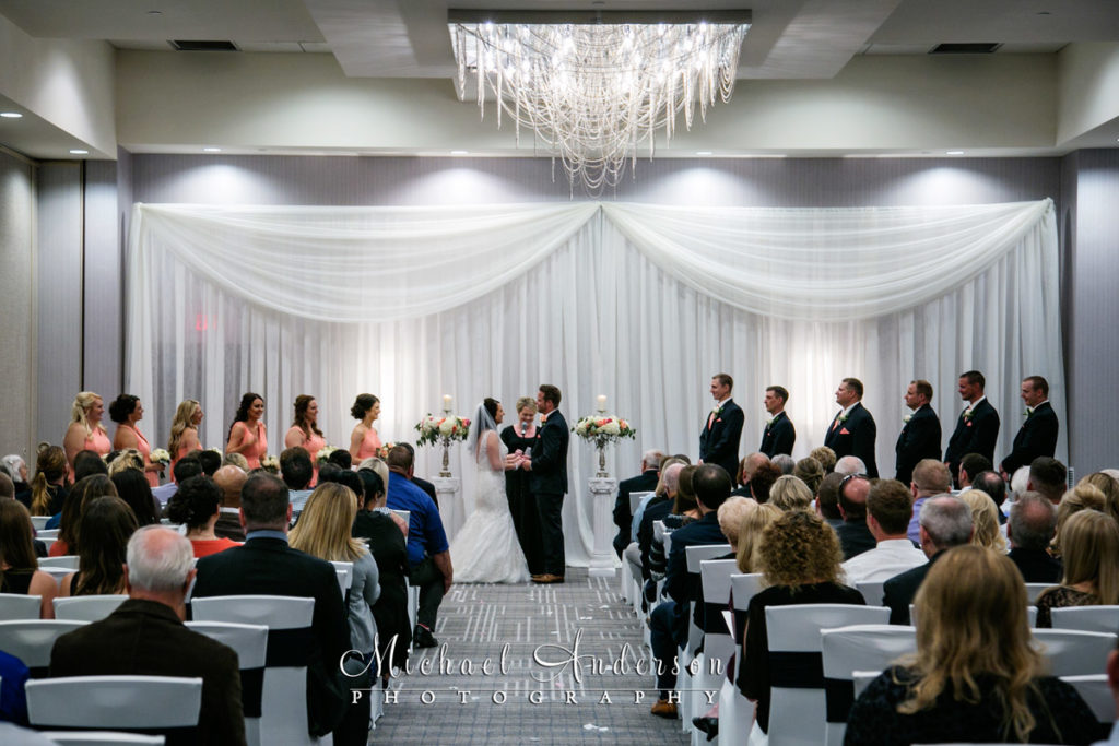 A wedding ceremony photograph of the bride and groom exchange their wedding vows in the pretty ballroom at the Hilton Minneapolis Bloomington.
