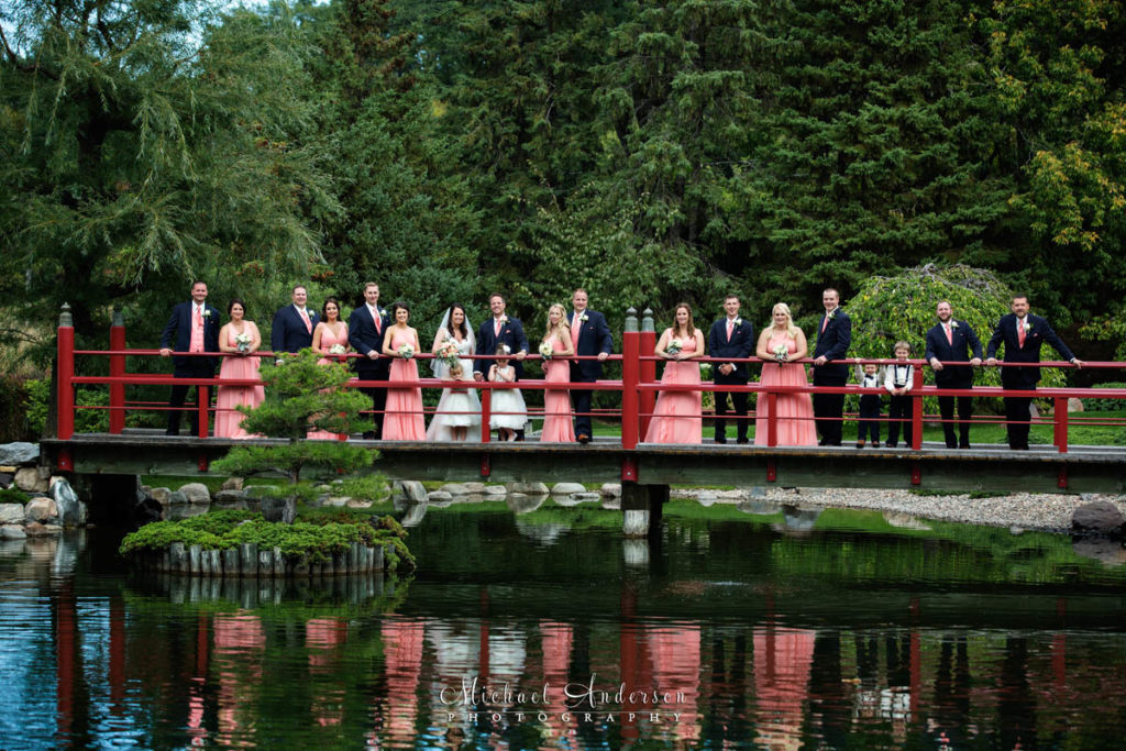 Wedding photography at The Japanese Garden at the Normandale Community College in Bloomington, MN. A fun wedding photograph of the bride, groom and their wedding party standing on a long, red bridge.