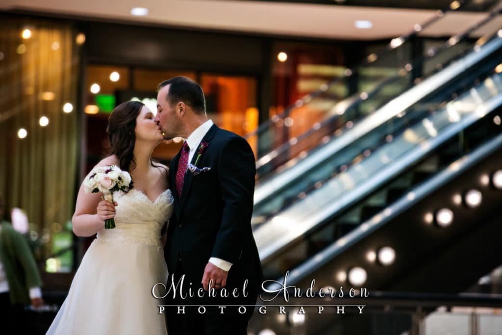 The bride and groom share a little kiss in the Crystal Court of the IDS Center in downtown Minneapolis, MN.