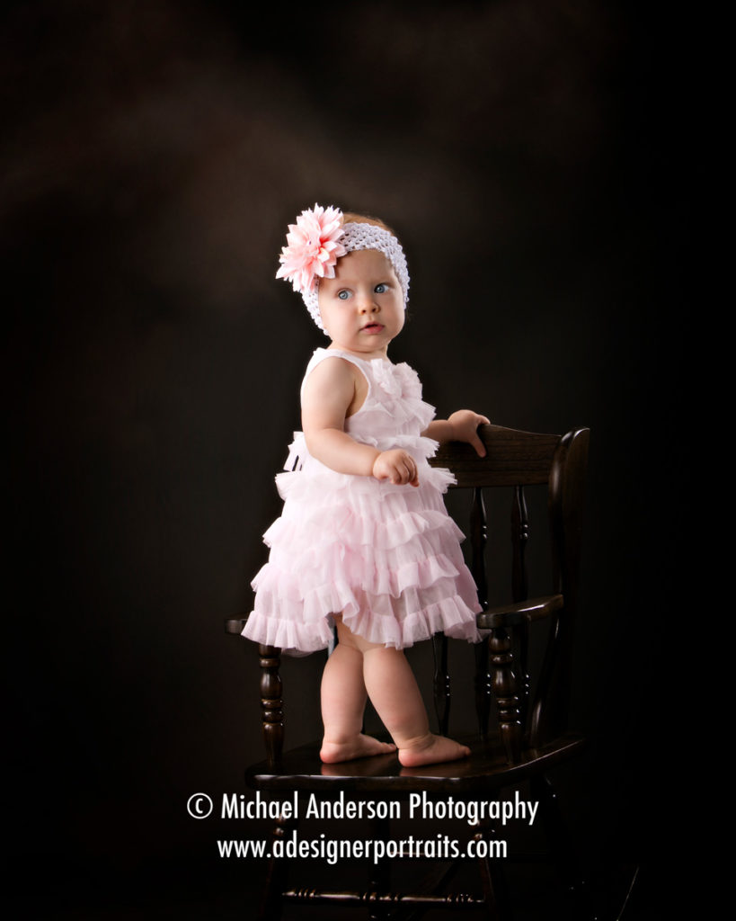 Katie's First Birthday Portraits. Katie is standing on her own rocking chair.