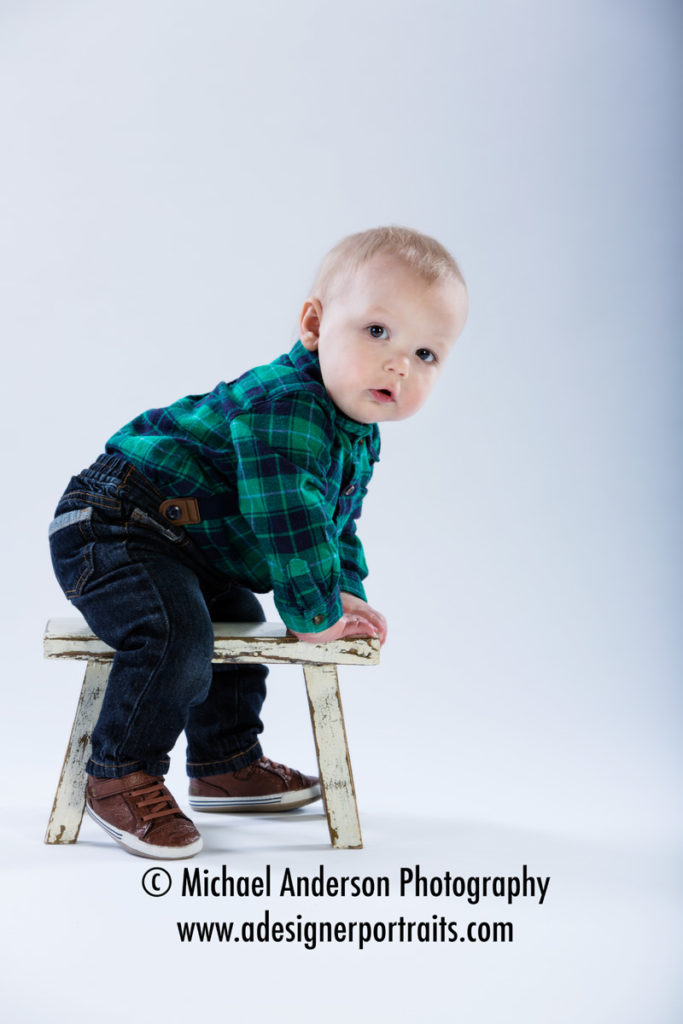 Cute little Noah's one-year-old portraits. He's sitting on a small bench.