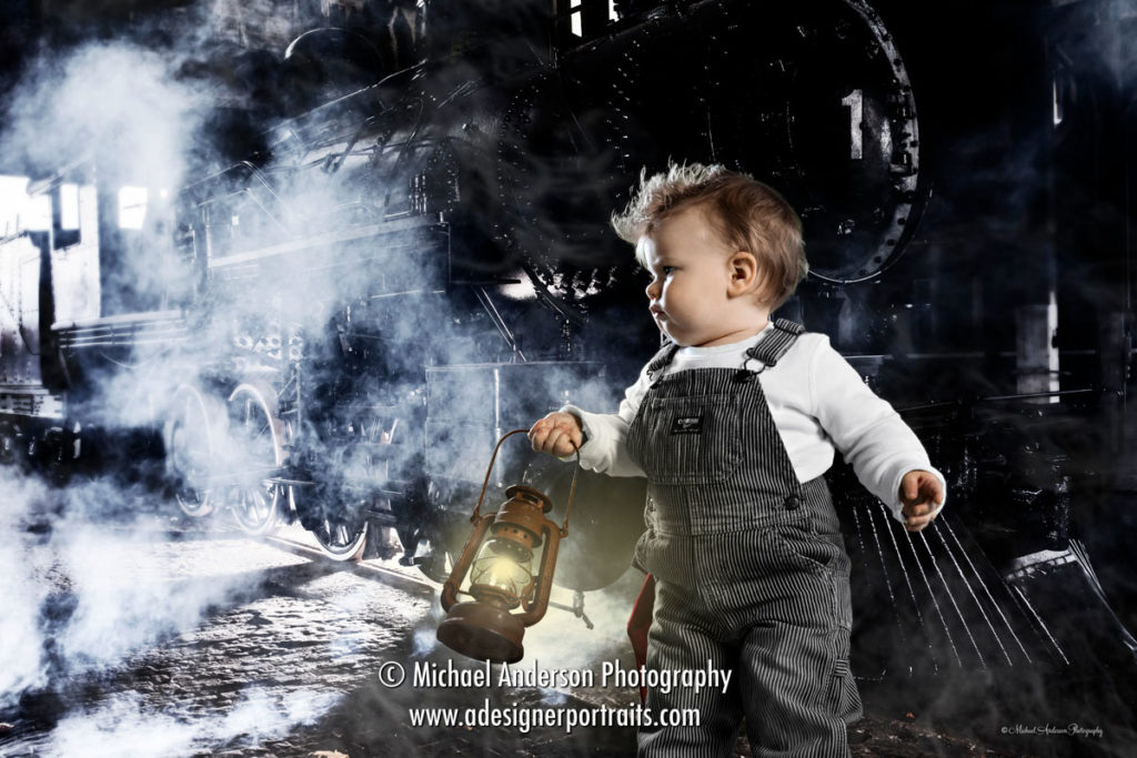 Baby Boy Train Engineer Photos. A super cute one year old baby boy holding a train lantern and dressed as a train engineer. A green screen composite photo with a steam locomotive at train station with dramatic lighting and lots of steam.