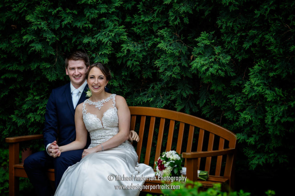 A bride and groom sitting on a bench in the pretty garden at The Saint Paul Hotel in St. Paul, MN.