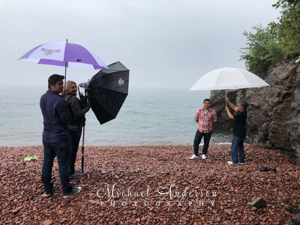 Behind-the-scenes photo of a high school senior being photographed in the rain on Lake Superior.