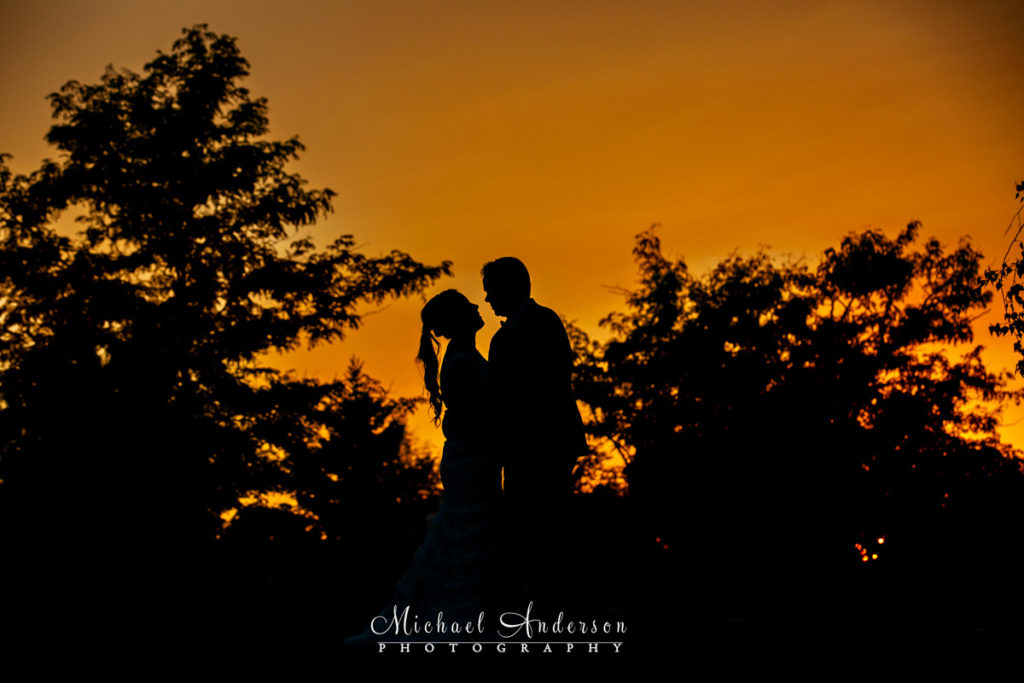 TPC Twin Cities wedding reception photos of a bride and groom kissing in silhouette at sunset.
