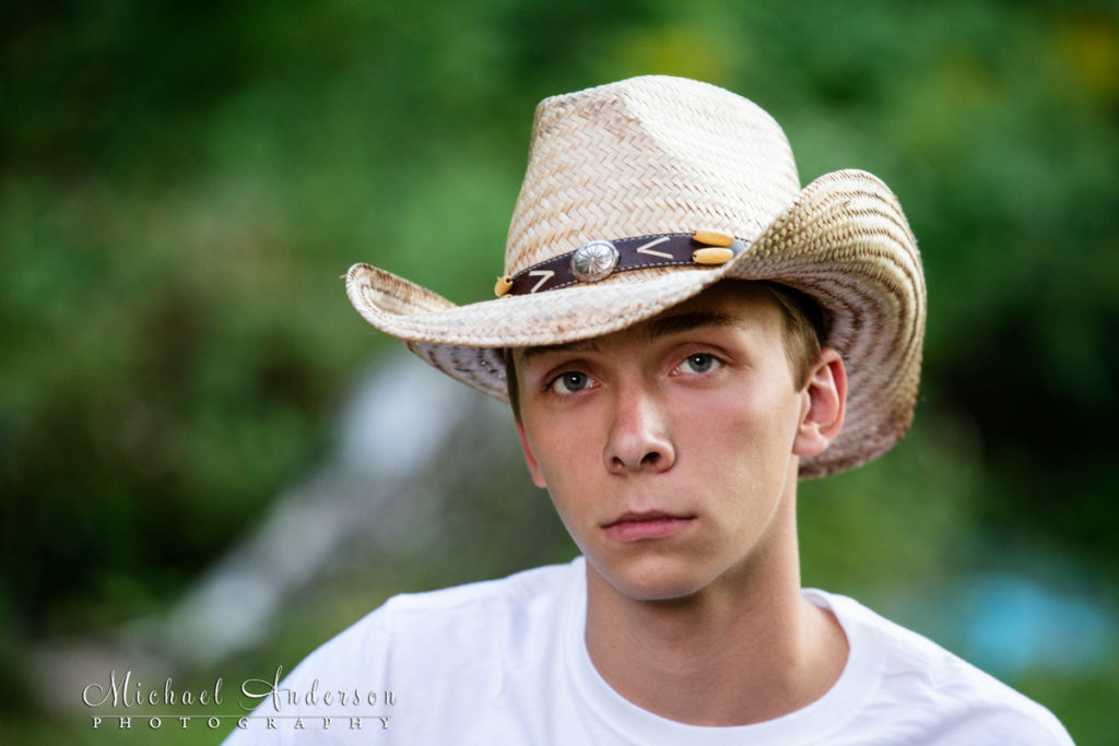 Tight close up high school senior portrait of a boy wearing a cowboy hat.