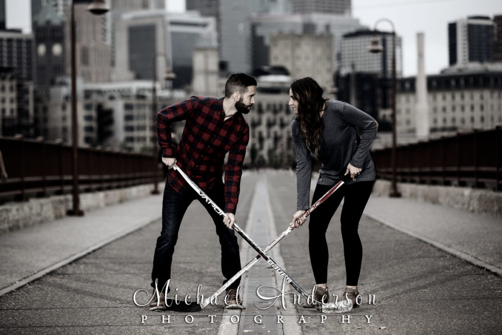 Saint Anthony Main engagement photos of a couple "facing-off" with their hockey sticks on the Stone Arch Bridge in Minneapolis, MN.