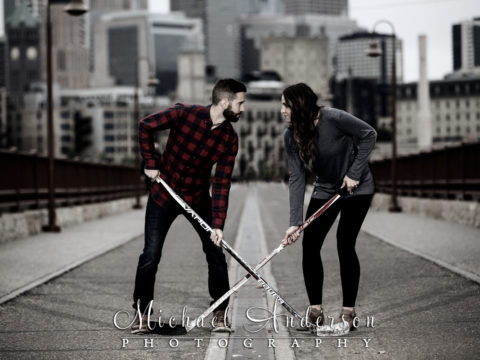 Saint Anthony Main engagement photos of a couple "facing-off" with their hockey sticks on the Stone Arch Bridge in Minneapolis, MN.