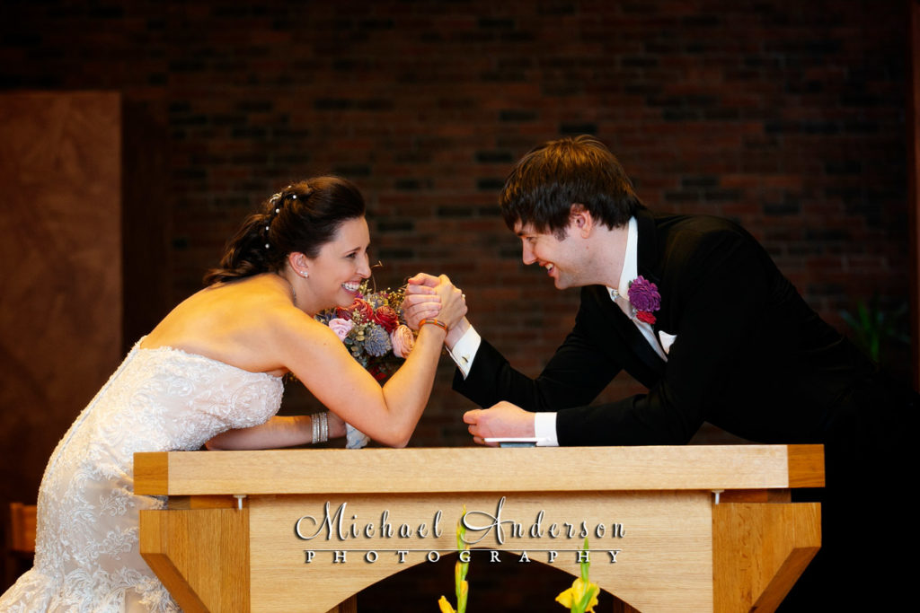 Fun Guardian Angels wedding photos of the bride and groom arm wrestling at the altar.