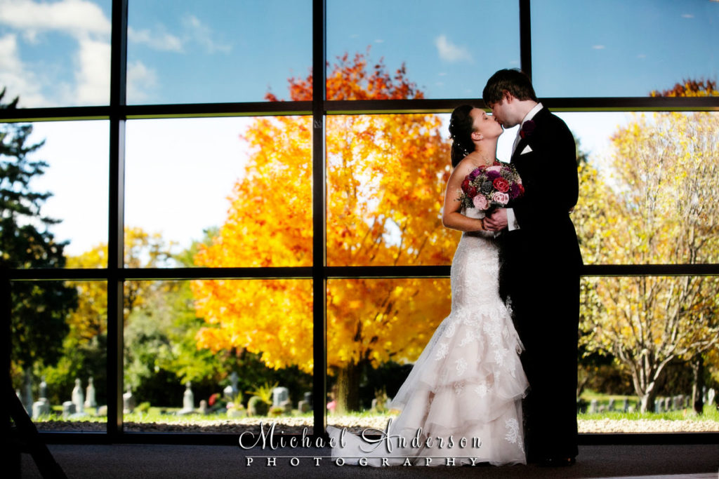 Guardian Angels wedding photos of a bride and groom in front of the large window with pretty fall colors in their background.