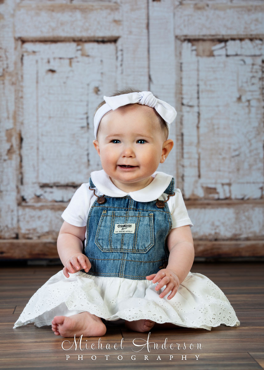 A simply adorable studio portrait of a nine-month-old baby girl wearing an OshKosh dress.