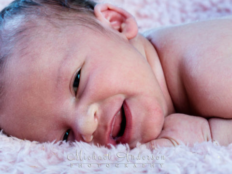 Cute little bugger newborn baby girl with a sweet little smile.