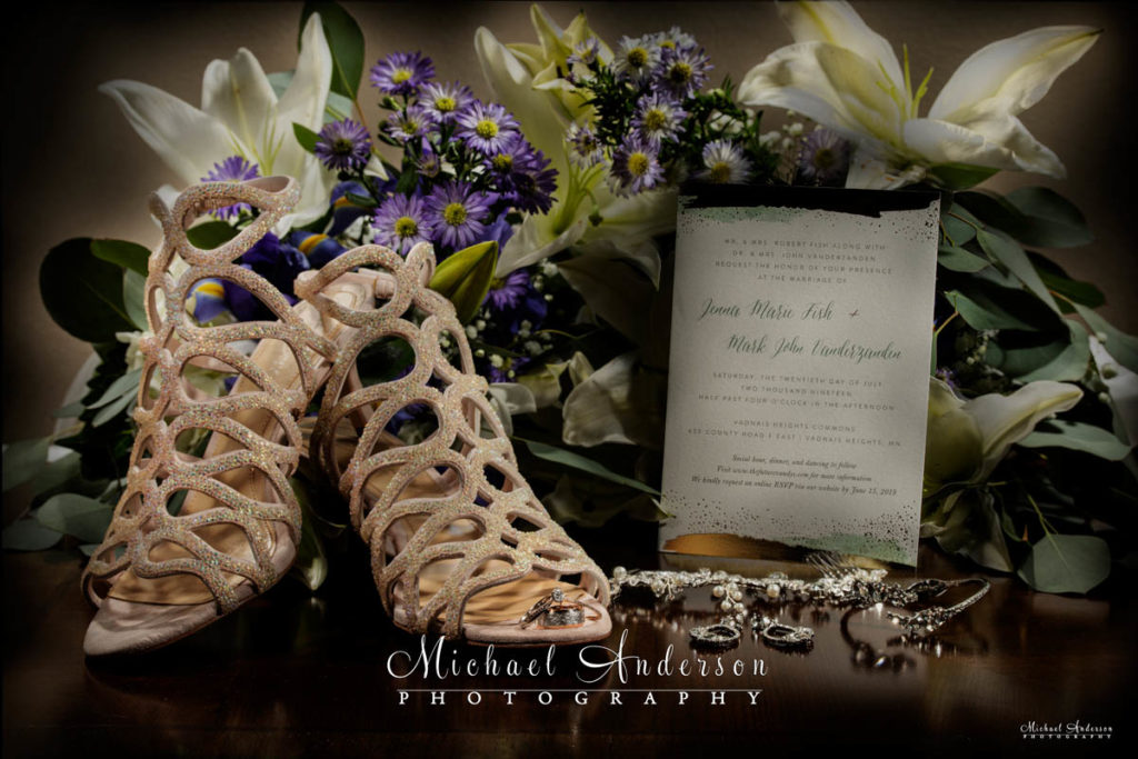 A pretty light painted wedding photo of the brides shoes, jewelry, wedding rings, flowers, and invitation.